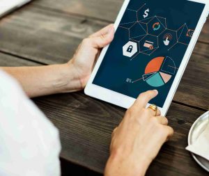 Uma pessoa segura um tablet que exibe gráficos coloridos e ícones financeiros, representando estratégias digitais de organização de dinheiro e gamificação nas finanças para estimular o alcance de metas com recompensas.