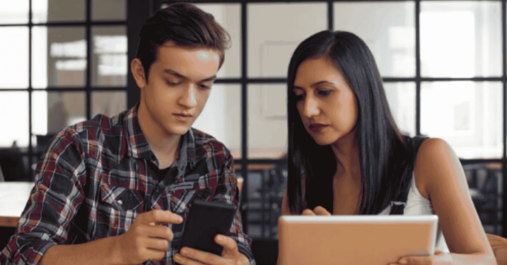Contas Digitais Com Foco Em Adolescentes: A Nova Fronteira Da Educação Financeira No Brasil 1 Um jovem e uma mulher sentados juntos em uma mesa, usando um smartphone e um laptop enquanto trabalham ou estudam.