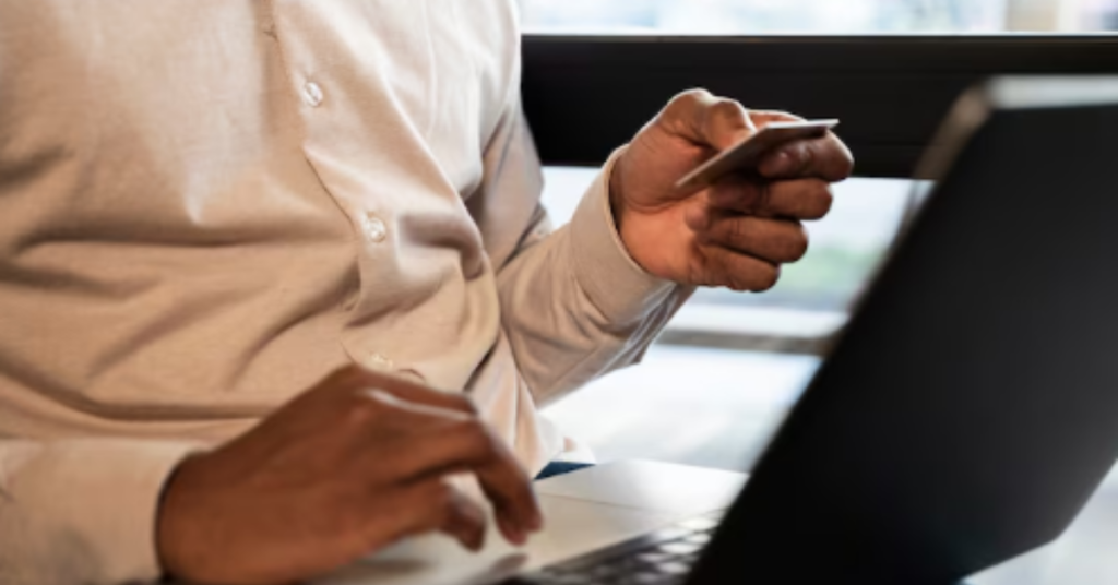 Pessoa segurando um cartão de crédito e usando um laptop para fazer uma compra online.